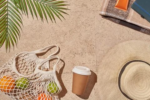 Summer sun beach concept flat lay.Hat, string bag with fruits, cup, palm leaves. Stock Photos