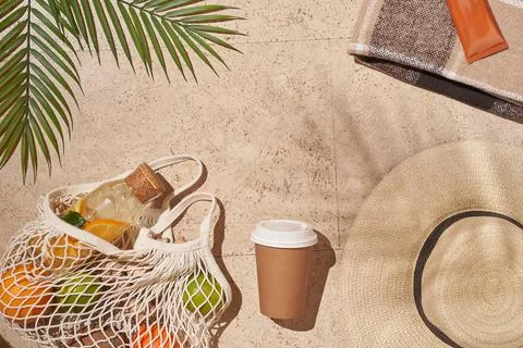 Summer sun beach concept flat lay.Hat, string bag with fruits, cup, palm leaves. Stock Photos