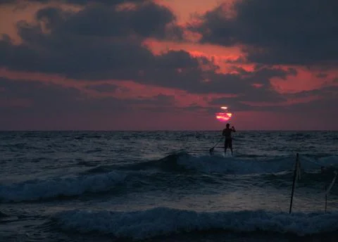 Summer sunset view of a beach under a cloudy sky with a single sup surfer Stock-Fotos
