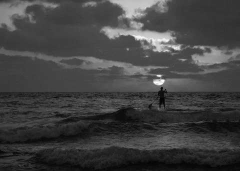 Summer sunset view of a beach under a cloudy sky with a single sup surfer 写真素材