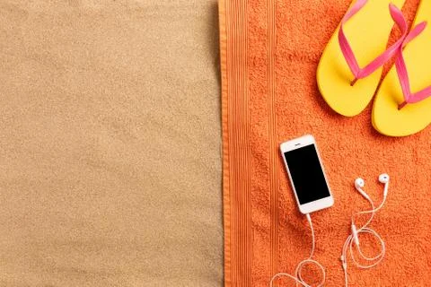 Summer vacation composition. Flip flops, smartphone and headphones on sand ba Stock Photos