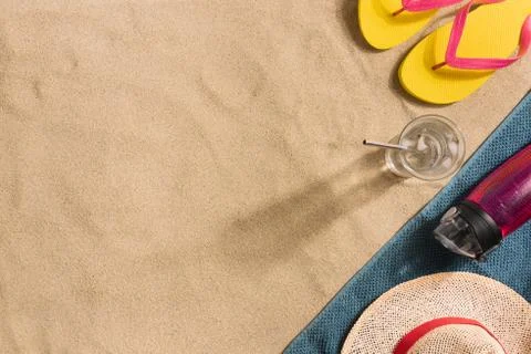 Summer vacation composition. Flip flops, water bottle and straw hat on sand b Stock Photos