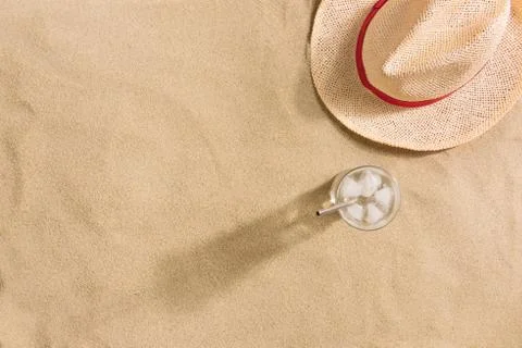 Summer vacation composition. Hat and glass of water with ice on sand backgrou Stock Photos
