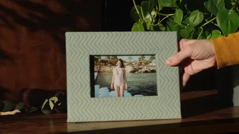 Summer vacation memories concept. Hand places photo frame on table. Stock Footage 240242102