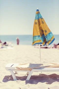 Summer vertical composition of a beach umbrella and deck chair with a carelessly Stock Photos