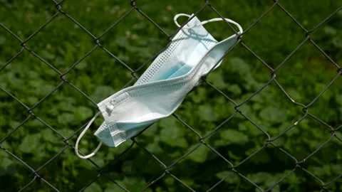 Summer wind blowing a blue surgery mask on wired garden fence Stock Footage 158370208
