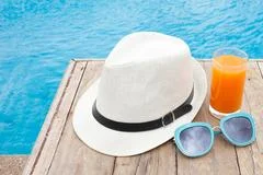 Beach hat, orange juice and sunglasses near the swimming pool