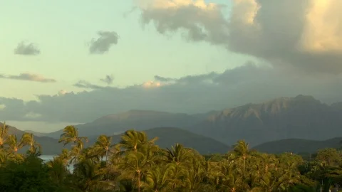 Sun and clouds hover over island mountains and palm trees A Stock Footage 125340865