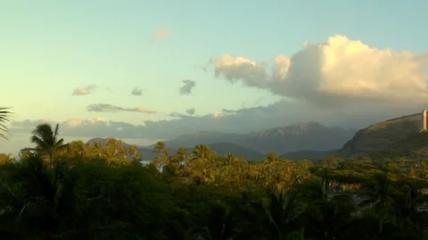 Sun and clouds hover over island mountains and palm trees B Stock Footage 125340901