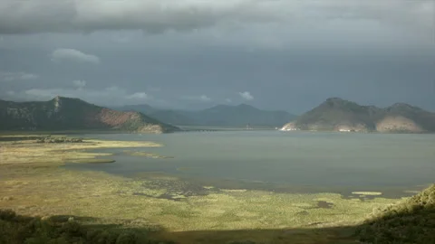 Sun and shadow on green meadow and a lake. Creative. Calm water and mountains on Stock Footage 254451244