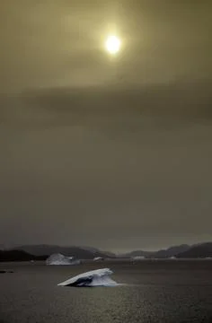 The sun appears among the clouds to dye with warm tones the sea with icebergs Stock Photos