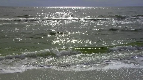 Sun backlights shimmering surf breaking on beach, sun reflects wave tops/horizon Stock Footage 70072383