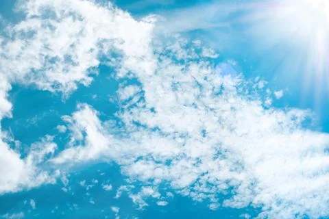 Sun beams lighting white clouds in bright blue sky Stock Photos
