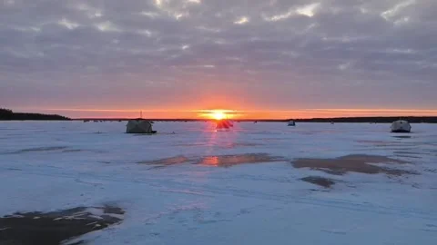 As the sun begins to set, its warm hues paint the sky above a serene, frozen lak Stock Footage 342581661