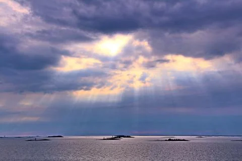 The sun behind the clouds with rays of light shining down on sea Stock Photos