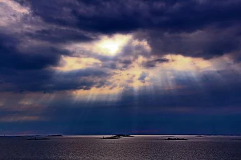 The sun behind the clouds with rays of light shining down on sea Stock Photos