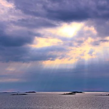 The sun behind the clouds with rays of light shining down on sea Stock Photos