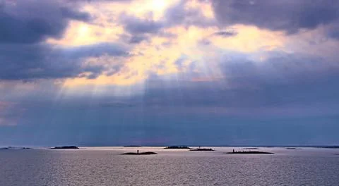 The sun behind the clouds with rays of light shining down on sea Stock Photos
