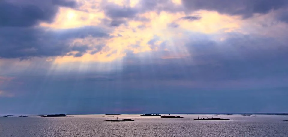 The sun behind the clouds with rays of light shining down on sea Stock Photos