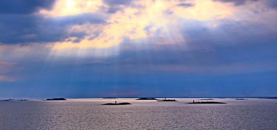 The sun behind the clouds with rays of light shining down on sea Stock Photos