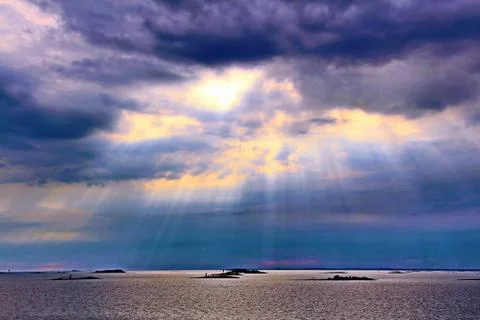 The sun behind the clouds with rays of light shining down on sea Stock Photos
