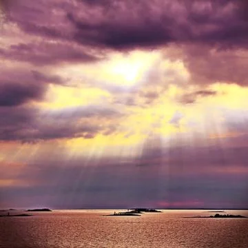 The sun behind the clouds with rays of light shining down on sea Stock Photos
