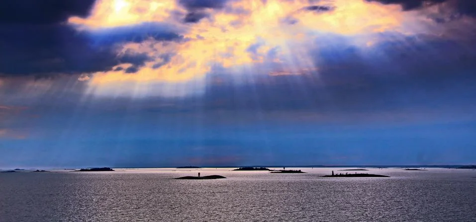 The sun behind the clouds with rays of light shining down on sea Stock Photos