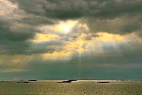 The sun behind the clouds with rays of light shining down on sea Stock Photos