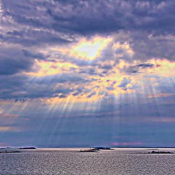 The sun behind the clouds with rays of light shining down on sea Stock Photos