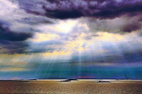 The sun behind the clouds with rays of light shining down on sea Stock Photos