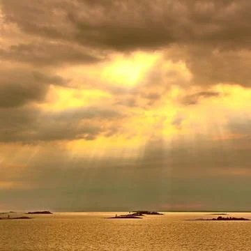 The sun behind the clouds with rays of light shining down on sea Stock Photos