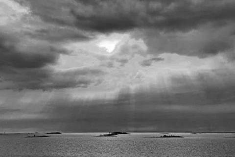 The sun behind the clouds with rays of light shining down on sea Stock Photos