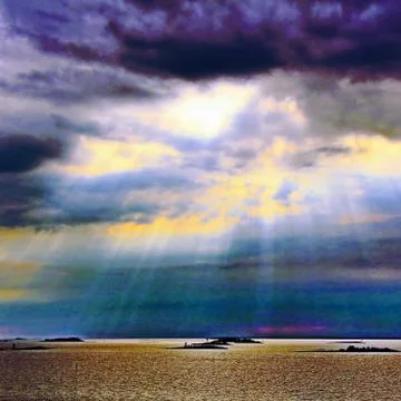 The sun behind the clouds with rays of light shining down on sea Stock Photos