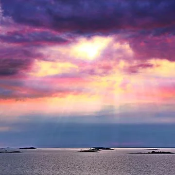 The sun behind the clouds with rays of light shining down on sea Stock Photos