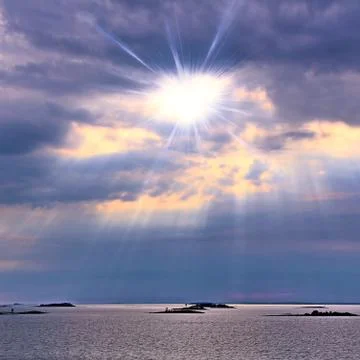 The sun behind the clouds with rays of light shining down on sea Stock Photos