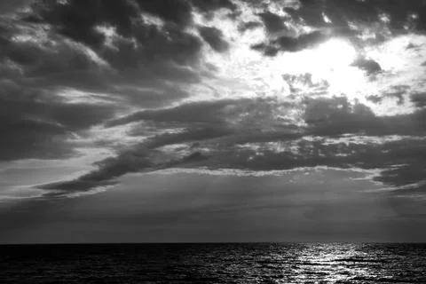 The sun behind the clouds, reflection of sunlight in the sea, black and white Stock Photos