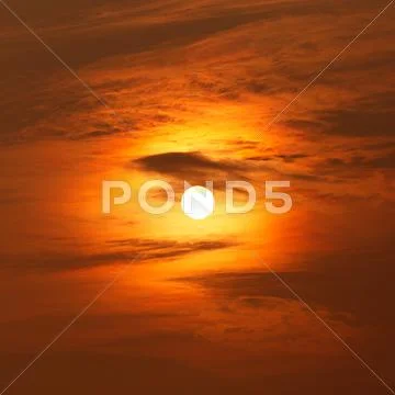 Sun behind clouds at sunset Stock Photos