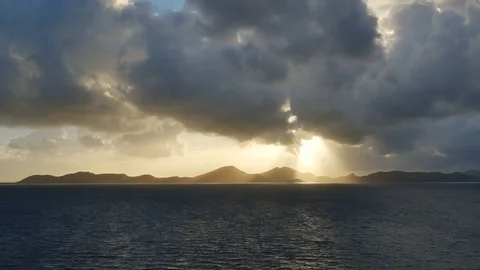 Sun behind dark clouds cast ray on island silhouette-Establishing shot-ZOOM Stock Footage 73712546