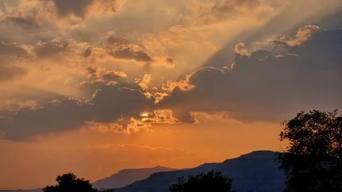 Sun behind dramatic clouds with sunray sky above the mountain range Stock Photos