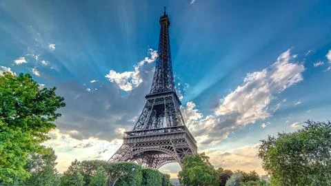 Sun behind the Eiffel tower with warm rays of light in clouds during sunset t Stock Photos