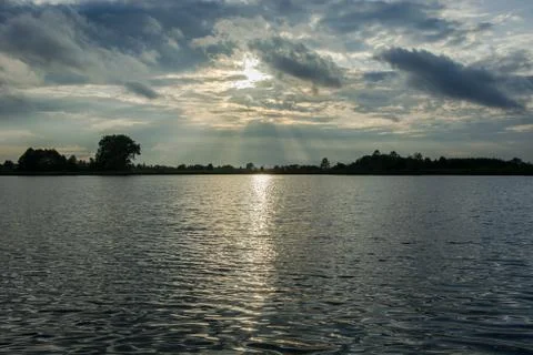 The sun behind rainy clouds and reflecting light in the water of the lake Stock Photos