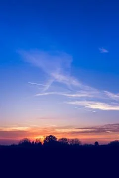 Sun behind trees at sunset with little clouds on blue sky Stock Photos