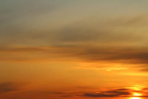 Sun below the horizon and clouds in the fiery dramatic orange sky at sunset or Stock Photos