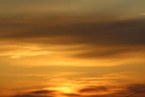 Sun below the horizon and clouds in the fiery dramatic orange sky at sunset or Stock Photos