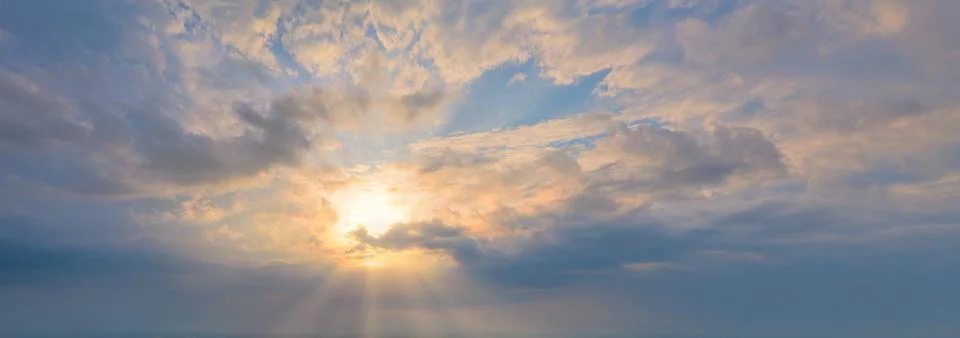 The sun in the blue sky with clouds. Rays shine through the clouds. Panoramic Stock Photos