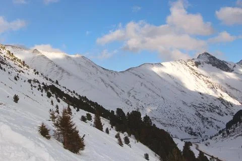 Sun is breaking through clouds. Alps peaks are covered with snow and forest Stock Photos