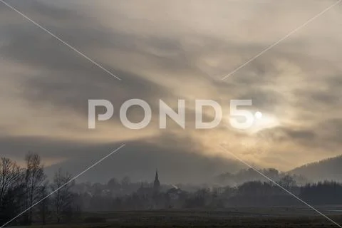 The sun breaking through the clouds just above the forest-covered mountains Stock Photos