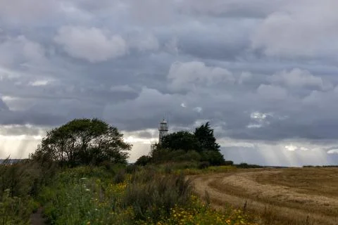 Sun breaking through clouds over lighthouse and wheat field Stock Photos
