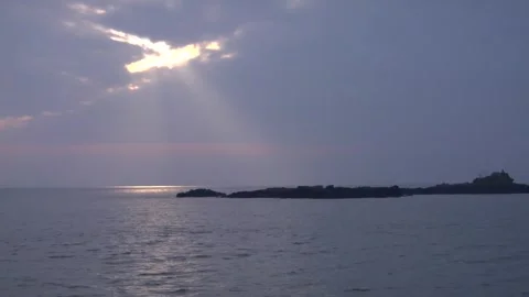 Sun breaking through clouds shining in rocky island Stock Footage 277528083