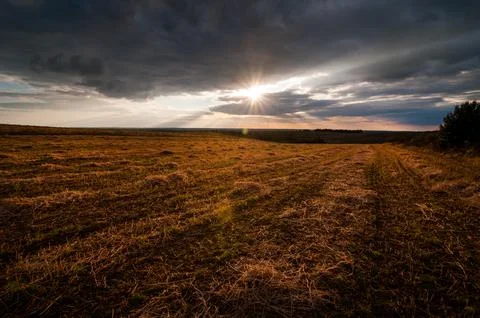 The sun breaks through the clouds, field with golden light after the harvest Stock Photos